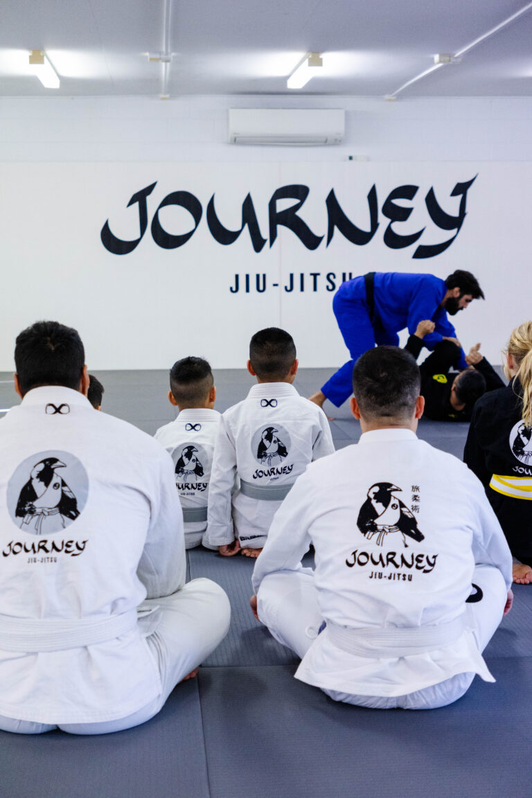 Coach demonstrating a Brazilian Jiu-Jitsu technique to parents and children.