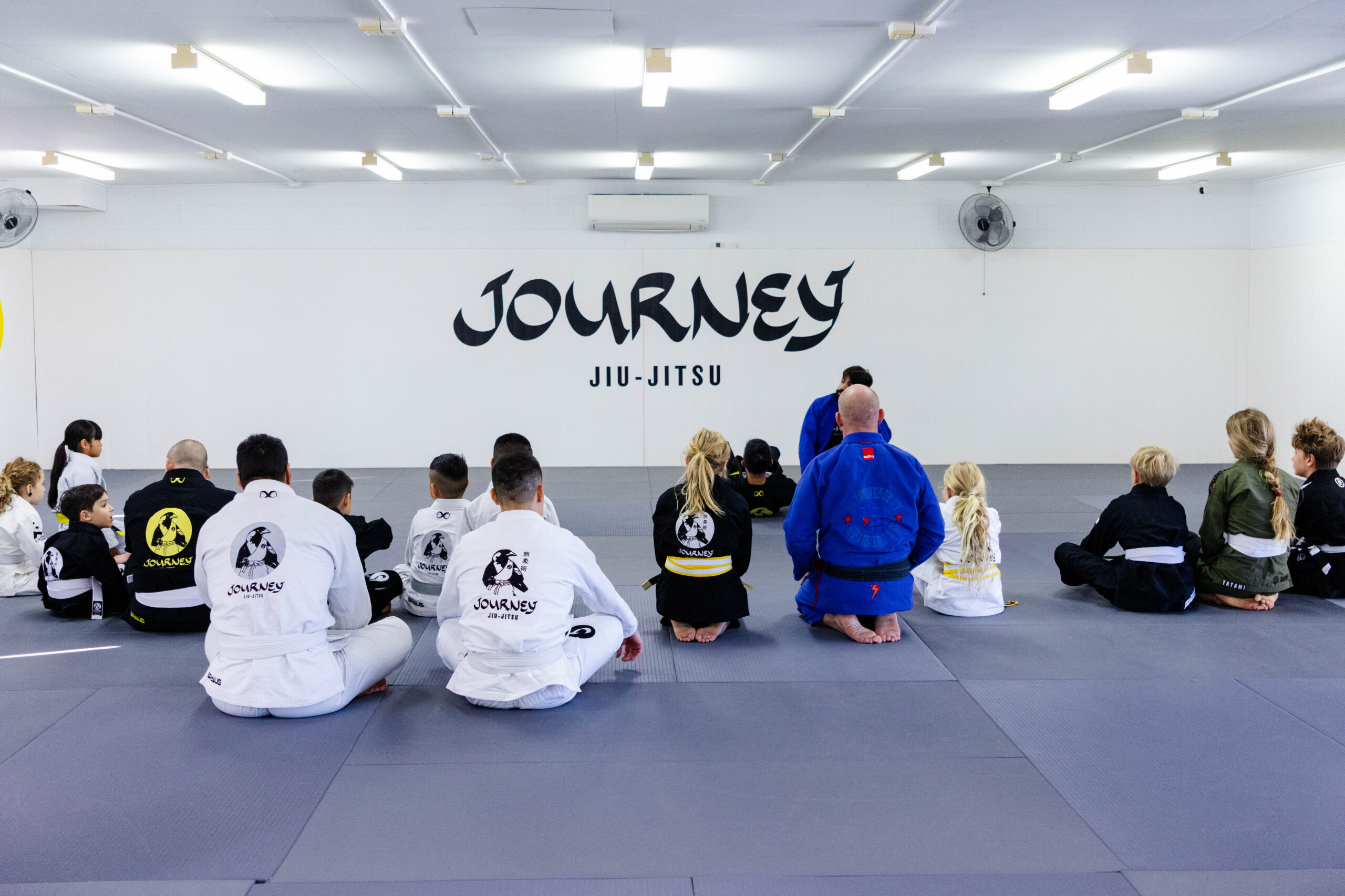 Coach demonstrating a Brazilian Jiu-Jitsu technique to parents and children.